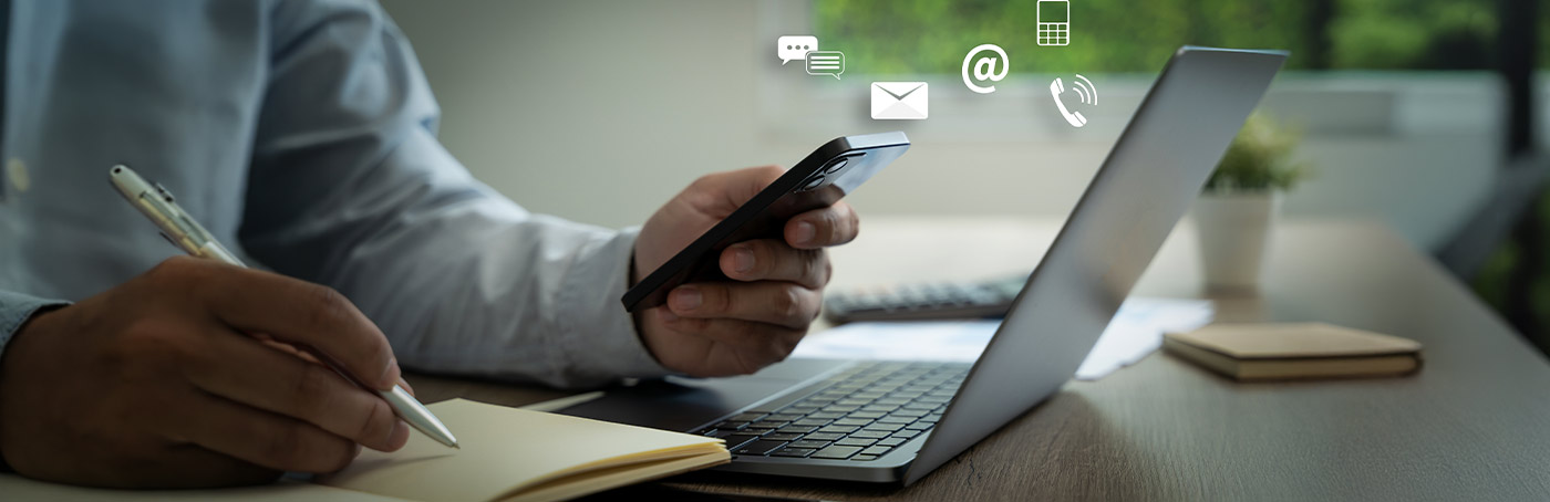 Image of a man writing down notes on a notepad while looking up information on his phone