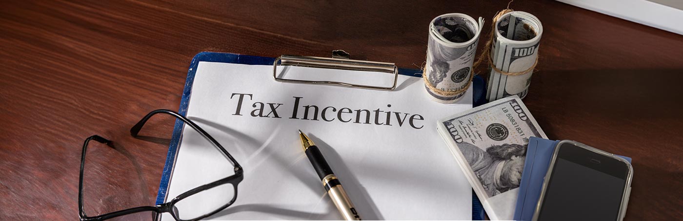 A picture of glasses, money, and a phone, sitting on top of a tax incentive sheet on a clipboard