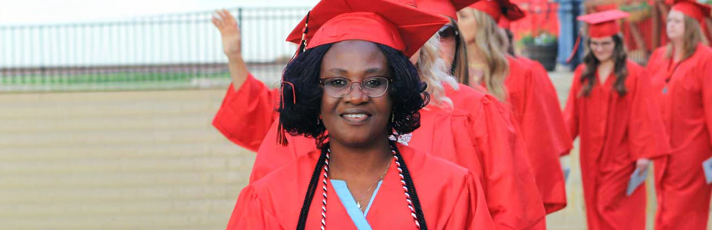 An African-American woman smiling in a red SCC graduation robe with fellow graduates behind her
