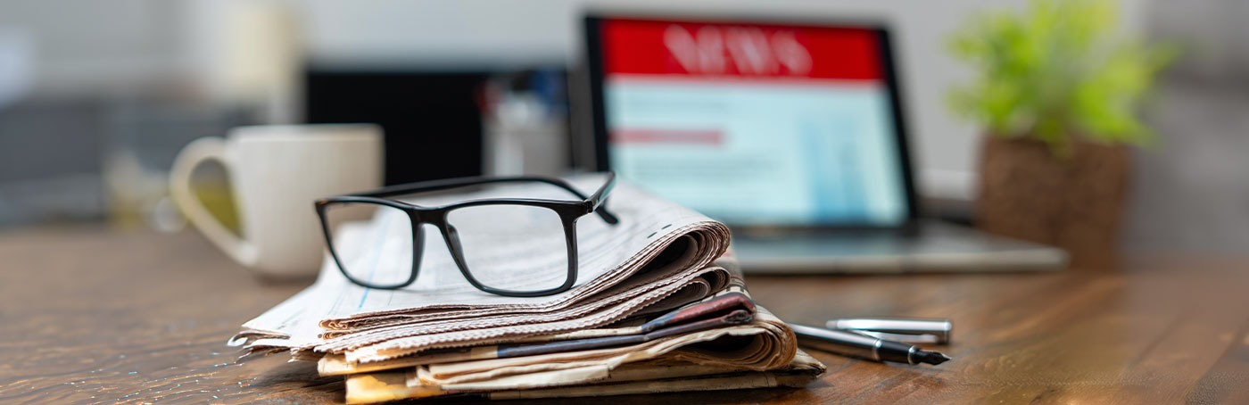 Glasses resting on a newspaper with a laptop in the background