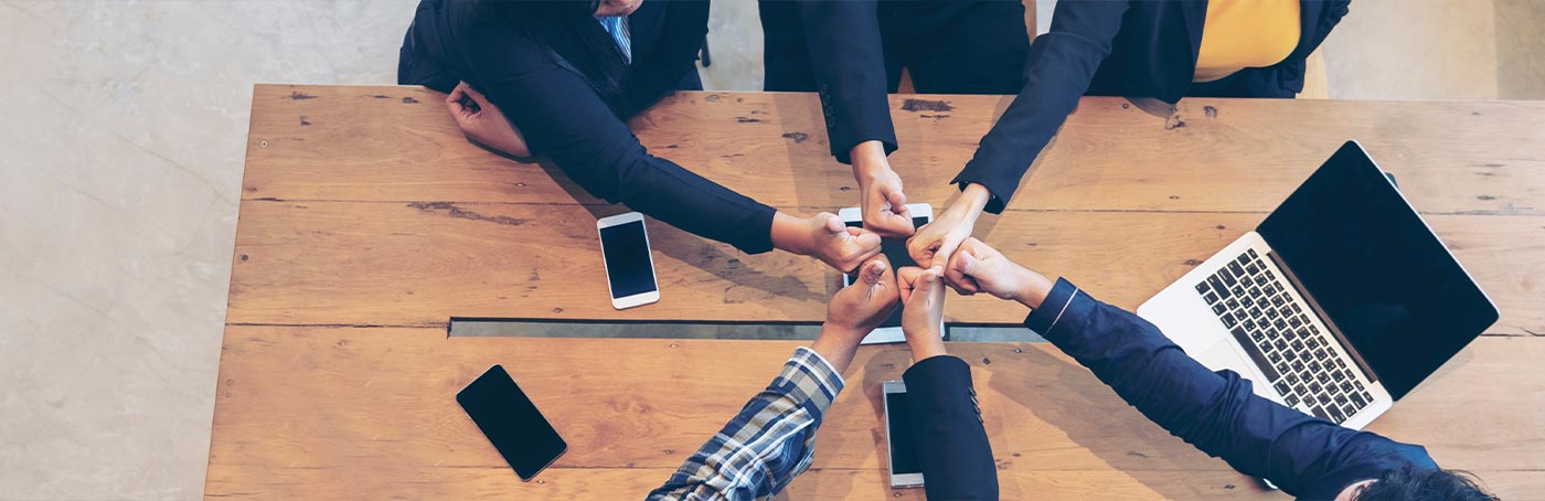 A group of people in business attire and their hands coming together with thumbs up on a table