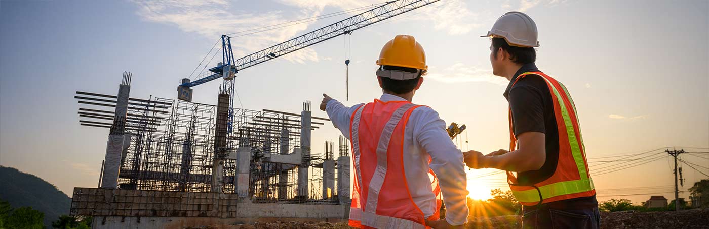 A construction foreman points to a building being constructed, and talks with a fellow employee on-site