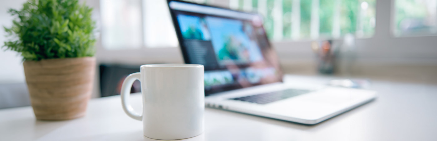 Image of a coffee cup and an open laptop sitting on a white table