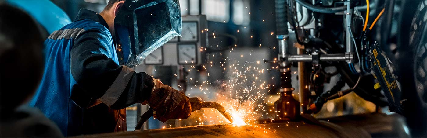 A close-up of a man in welding gear, sautering a metal tank