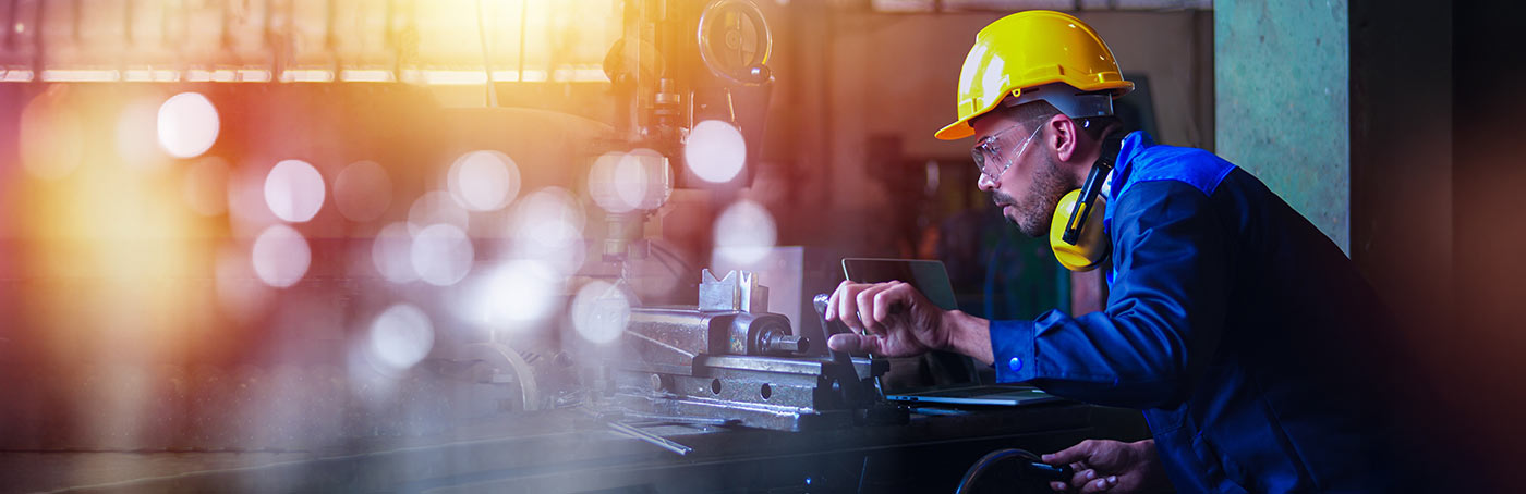 A man in a hard hat concentrates as he operates manufacturing equipment